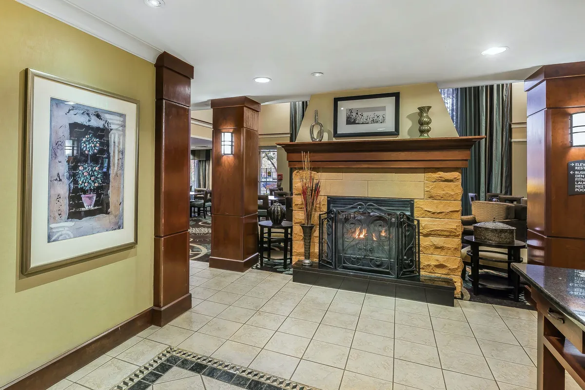 A cozy seating area centered around a warm fireplace, framed art, and comfortable chairs. The setting invites guests to relax, socialize, or enjoy a quiet moment, reflecting both community and individual leisure possibilities.
