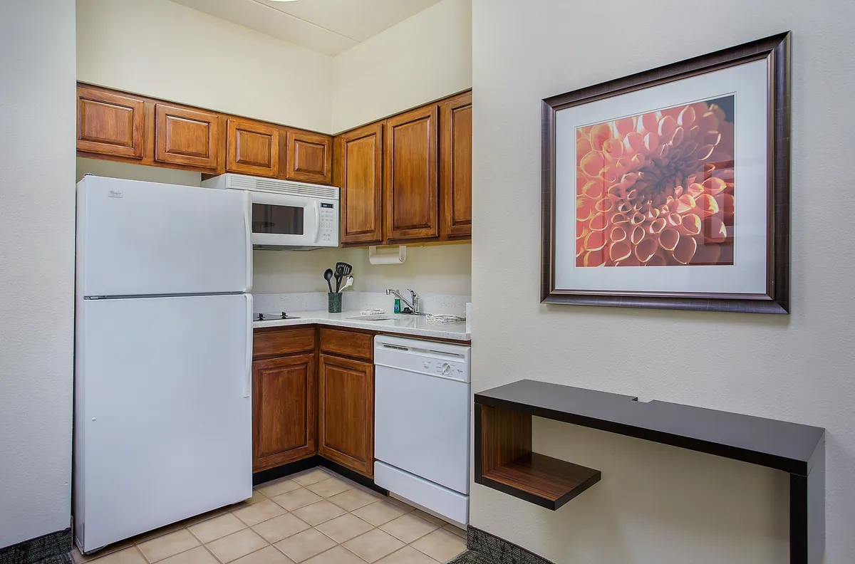 A cozy kitchen space equipped with a refrigerator, microwave, dishwasher, and decorative wall art. The intimate layout suggests an inviting spot for cooking or gathering, with thoughtful design details.