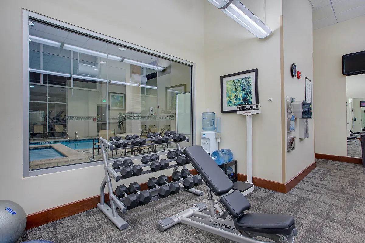 This image features a well-equipped fitness center with a dumbbell rack, weight bench, water cooler, and vibrant wall artwork. The space is bright and inviting, supporting activities such as strength training, group fitness, and post-workout relaxation.