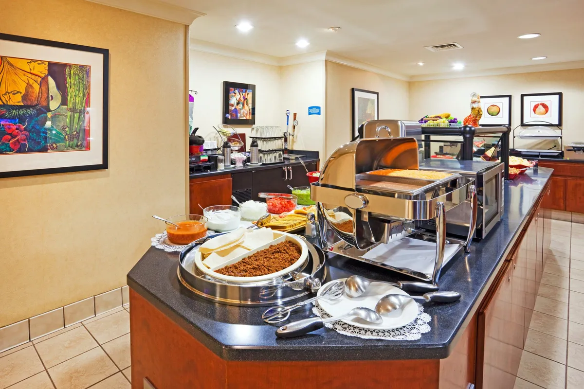 A welcoming buffet area with a well-stocked table, coffee station, and decorative artwork. Guests are seen serving themselves, emphasizing the ease and independence of self-catering. The scene connects food preparation with communal enjoyment.