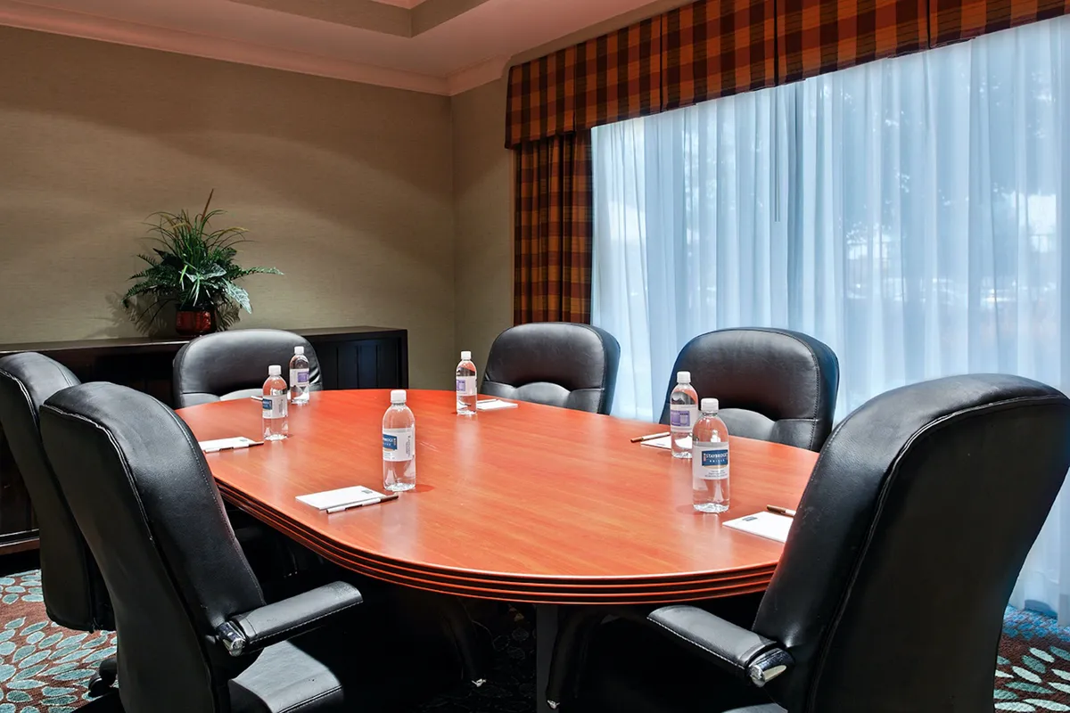 This image features an interior conference space with an oval wooden table surrounded by black leather chairs. Water bottles and notepads are neatly arranged, suggesting a professional, collaborative environment prepared for business gatherings or planning sessions.