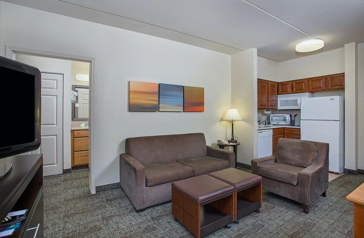 A comfortable living area with a modern sofa, striking artwork on the wall, and a view of the kitchen area in the background. The setting is designed for both relaxation and socializing, with decor that feels warm and inviting.